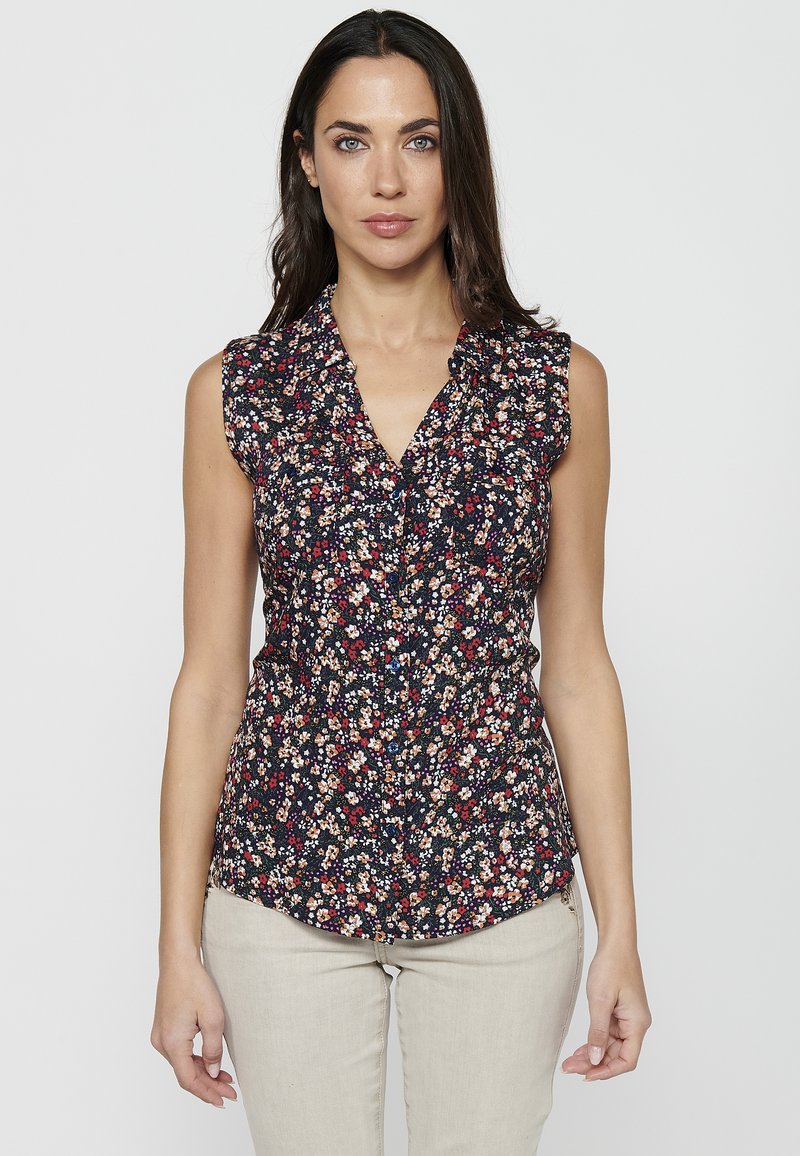 Blusa senza maniche floreale di colore blu scuro, con collo a camicia, dettagli arricciati alle spalle e piccoli motivi floreali multicolori.