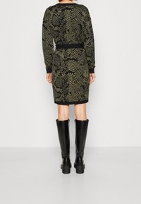 Abito in maglia con un motivo a serpente nero e verde oliva, scollo a girocollo, maniche lunghe e vita aderente con polsini e orlo a costine.