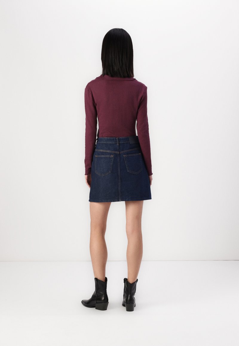 Burgunderfarbener, gerippter Langarm-Top kombiniert mit einem dunklen Jeans-Minirock. Der Rock hat Gesäßtaschen und eine strukturierte Oberfläche. Schwarze Knöchelstiefel.