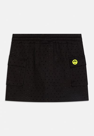 Black perforated mini skirt with elastic waistband, two large side pockets, and a small yellow circular patch with black design on right pocket.