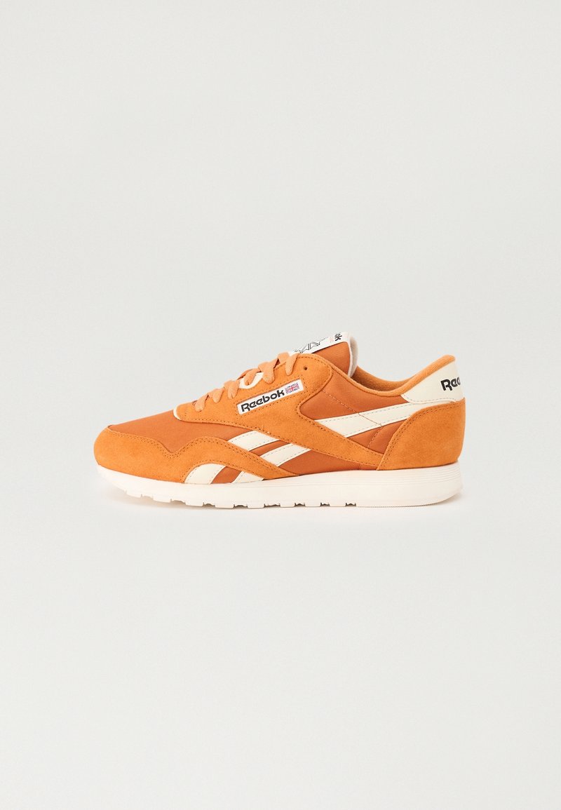 Baskets Reebok orange avec des bandes blanches, un lacet et une semelle blanche, vues de profil sur fond uni.