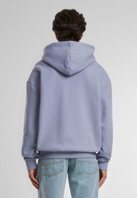 Lys lilla hettegenser med avslappet passform, ribbede mansjetter og kant, sammen med lyseblå denimjeans med baklommer.