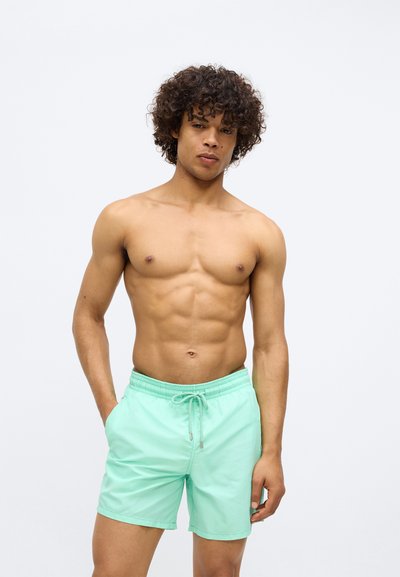 Μίντ πράσινα μαγιό με ελαστική μέση και κορδόνι, με απαλή υφή και πλαϊνές τσέπες, σχεδιασμένα για εφαρμοστή εμφάνιση.