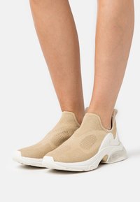 Chaussures beiges à enfiler tricotées avec un design texturé, semelle blanche unie et accents en mesh prononcés. Convient pour une tenue décontractée.
