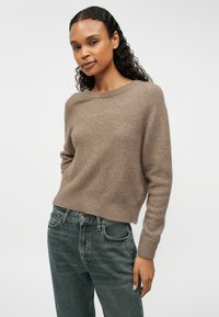 Brūns, mīksts adījuma džemperis ar plašu apļveida kakla izgriezumu un ribotām piedurknēm, apvienots ar nodiltiem zilu džinsiem. Vienkāršs, ikdienas dizains.