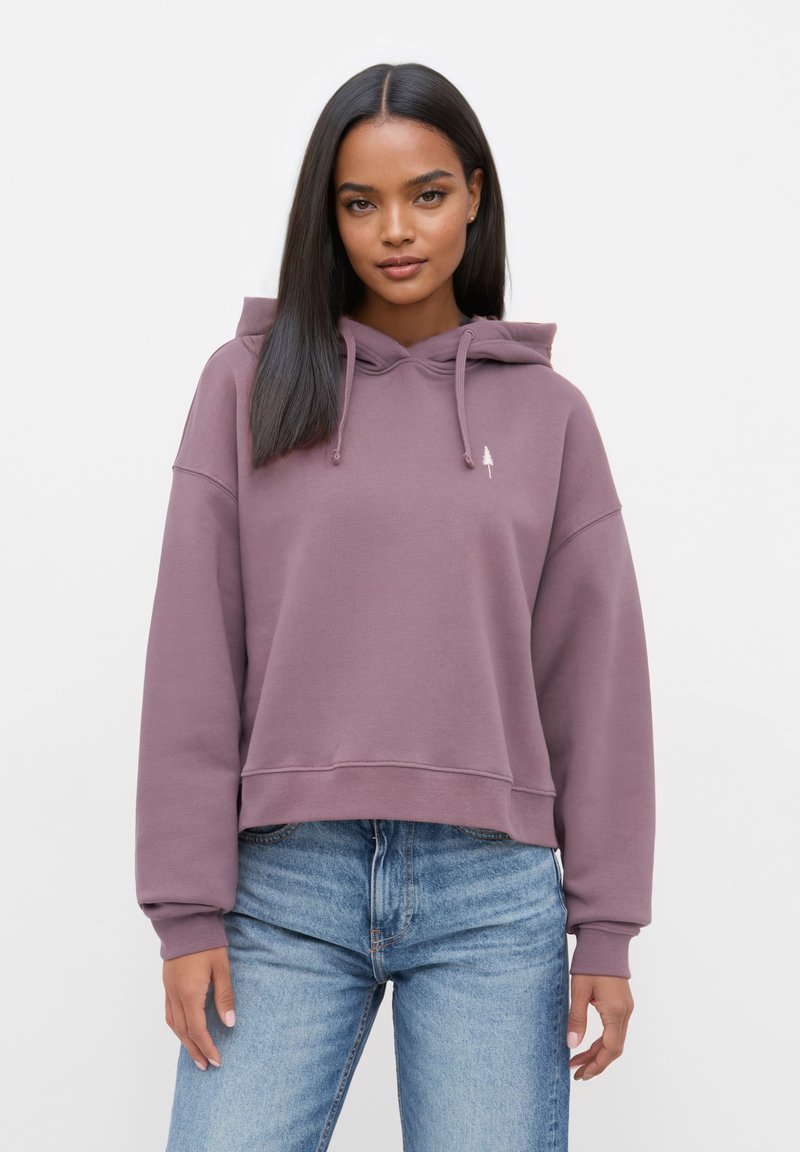 Paarse cropped hoodie met een trekkoordcapuchon, geribbelde manchetten en een klein boomlogo op de borst. Gecombineerd met blauwe jeans.