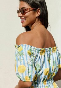 El vestido de hombros descubiertos presenta un patrón a rayas azul y blanco con acentos florales amarillos, incluyendo limones. Tela ligera con detalles elásticos.