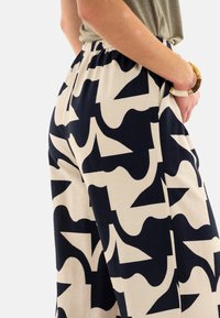 Pantalones con patrones en azul marino y beige con formas abstractas, que cuentan con una cintura elástica y un corte relajado. Tejido suave con una ligera textura.