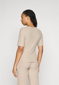 T-shirt beige à rayures avec des manches courtes, design ajusté et encolure ronde, associé à un pantalon à rayures assorti, mettant en avant une texture lisse.