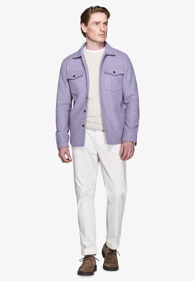 Lyslilla uldjakke med to brystlommer, båret over en cremet strikket sweater, sammen med hvide bukser og brune snørebåndssko.
