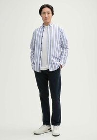 Gestreept shirt in blauw en wit, met een knoopsluiting en een relaxte pasvorm. Draag over een witte T-shirt met donkere broeken en witte sneakers.