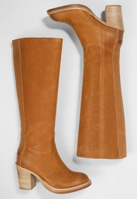 Botas de cuero marrón hasta la rodilla con tacón cuadrado. Cuentan con un acabado texturizado, paneles laterales elásticos y un detalle de diseño cosido.