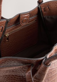 Intérieur d'un sac fourre-tout en cuir marron embossé crocodile, avec une poche zippée et une doublure lisse. La quincaillerie visible comprend une fermeture éclair dorée.