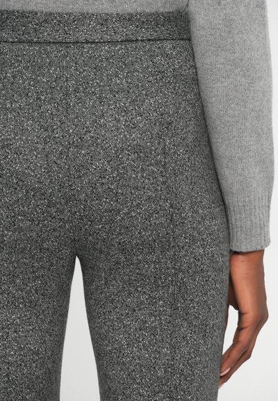 Pantalons tissés gris en tissu texturé. Présentent une taille ajustée et un motif chevron subtil, associés à une manche de pull gris clair.