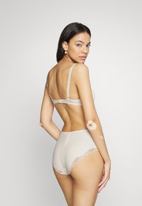Beige bra and high-waisted brief set with lace trim. Soft fabric, adjustable straps, and subtle sheen. View from the back.