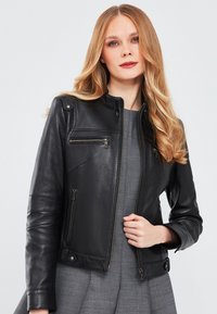 Zwarte leren jas met een ritssluiting aan de voorkant, zijzakken en drukknopen. Kenmerkt zich door een slim fit ontwerp en een gladde textuur met subtiele stiksels.