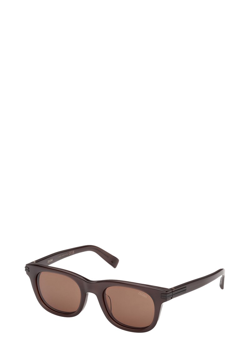 Brązowe plastikowe okulary przeciwsłoneczne z kwadratowymi soczewkami. Charakteryzują się smukłą oprawką i subtelnie teksturowanymi zausznikami. Soczewki z brązowym zabarwieniem zapewniają ochronę przed słońcem.