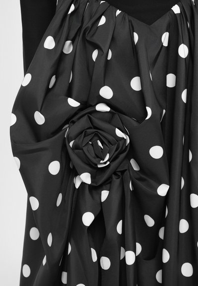 Mustast kangast valgete täppidega, millel on struktureeritud roosi meenutav detail ja voltitud tekstuur, rõhutab voolavust ja kontrasti.