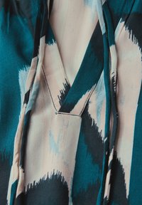 Tissu à motifs présentant des teintes de bleu canard, de noir et de rose clair dans un design abstrait ; texture lisse avec un léger éclat ; détails de couture visibles.
