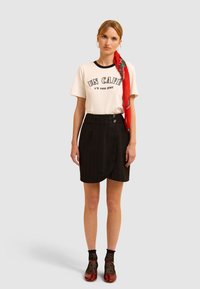 Witte T-shirt met zwarte rand en tekst, zwarte gestreepte rok, rode sjaal, zwarte visnet sokken en rode schoenen. Eenvoudig ontwerp, casual outfit.