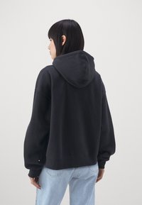 Sudadera negra de gran tamaño con capucha, que presenta mangas holgadas y una textura suave, combinada con jeans de mezclilla azul claro. Diseño simple y minimalista.