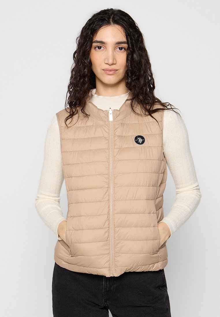 Beige gepolsterte Weste mit hohem Kragen, Reißverschluss auf der Vorderseite und Logopatch auf der linken Brust. Der Stoff ist glatt mit einem gesteppten Muster.