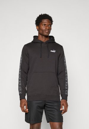Zwarte hoodie van katoen, met een kangoeroezak en een capuchon met trekkoord. De zijkanten van de mouwen hebben een bedrukt wit merklogo. Gecombineerd met zwarte shorts.