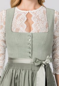 Grüner strukturierter Oberteil mit Spitzenärmeln, ausgestattet mit einem Schlüsselloch-Ausschnitt und silbernen Knöpfen. Ein Satinband in der Taille rundet das Design ab.