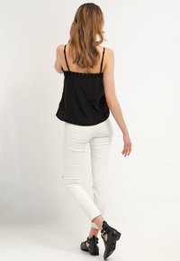 Black sleeveless top with adjustable straps, paired with white skinny jeans featuring slight distressing, and black ankle shoes with a buckle.