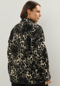 Czarna i beżowa kurtka w panterkę z miękką, teksturowaną powierzchnią; luźny krój i wysoki kołnierz; obniżone ramiona; zaokrąglony dół.
