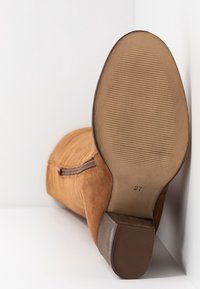 Bottine en daim marron clair avec fermeture éclair latérale, semelle inclinée indiquant la taille 37, petit talon empilé et semelle extérieure en caoutchouc texturé.