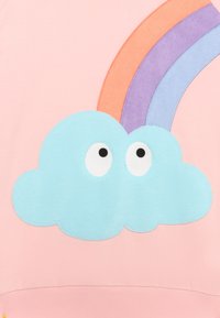 Sudadera rosa con una nube azul que tiene grandes ojos blancos y un arcoíris en naranja, púrpura y azul, hecha de una tela suave con acentos texturizados.