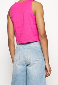 Fuchsie zkrácený top bez rukávů vyrobený z bavlny, s kulatým výstřihem, doplněný světle modrými džíny s vysokým pasem.