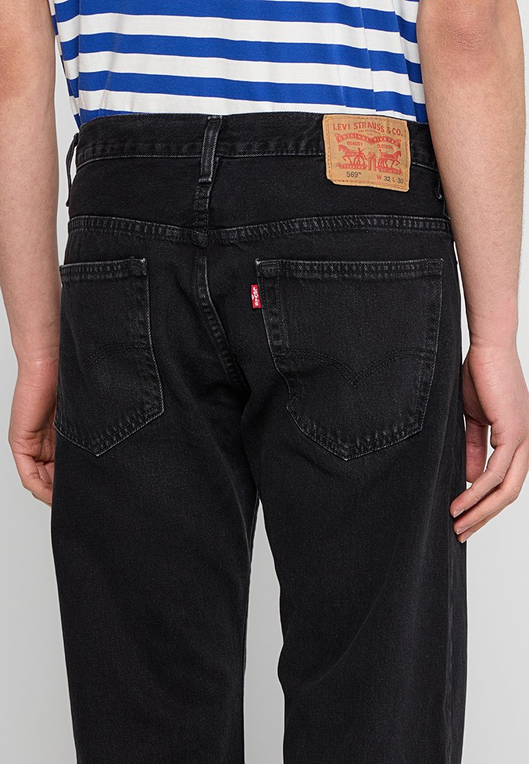 Czarne dżinsy typu denim z lekkim przetarciem, posiadające tylne kieszenie oraz charakterystyczną czerwoną metkę marki Levi's. Pas wykonany jest z brązowej skóry.