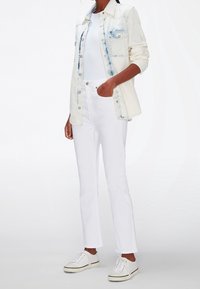 Jeans blancos y una chaqueta de mezclilla clara con acentos azules, combinados con una blusa blanca de manga corta y zapatillas blancas.