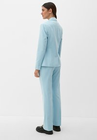 Abito azzurro chiaro composto da un blazer sartoriale e pantaloni dritti, realizzato in tessuto testurizzato, abbinato a calzature nere robuste.