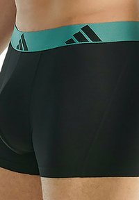 Svarta atletiska boxertrosor med en turkos midja som har svarta logotypstripes. Tyget ser slätt ut med en åtsittande design.