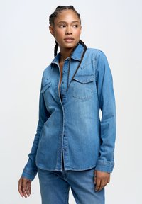 Hellblaues Jeanshemd mit langen Ärmeln, zwei Brusttaschen und einer Knopfleiste. Weicher Stoff mit einer leicht lockeren Passform.