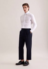 Weißes Hemd mit langen Ärmeln und Knopfleiste, kombiniert mit marineblauer Hose, mit Falten und schwarzen eleganten Schuhen. Glatter Stoff mit tailliertem Design.