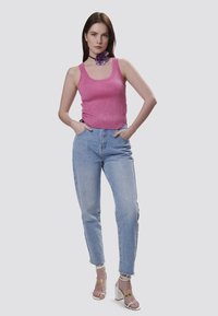 Top corto rosa con paillettes, jeans chiari a vita alta con orlo strappato e sandali trasparenti con tacco a blocco. Accessorio floreale al collo.