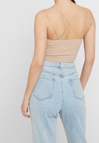 Ljusbrun ribbad croptop med tunna korsande axelband. Matchad med högmidjade blekta blå jeans med bakfickor.