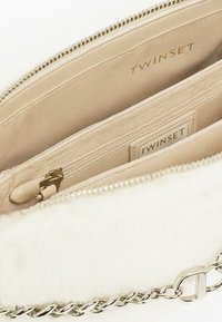 Borsa beige con esterno in morbido pelliccia testurizzata, tracolla a catena e chiusura a zip. L'interno presenta tessuto beige e scomparti multipli.