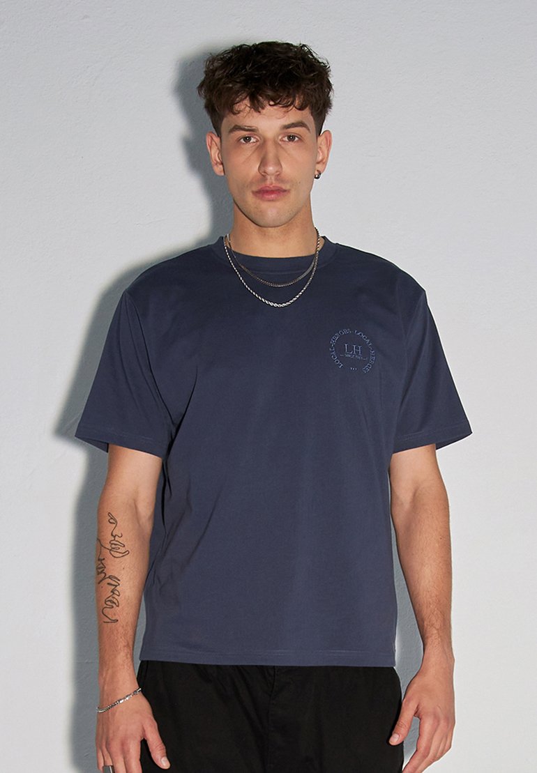 Granatowa bawełniana koszulka z luźnym fasonem, krótkimi rękawami i okrągłym dekoltem. Zawiera mały detal z logo na lewej piersi.