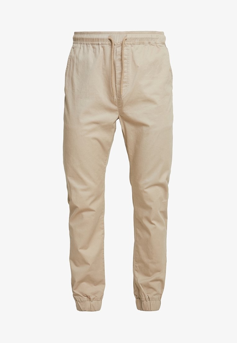 Pantalon décontracté beige avec taille élastique, fermeture par cordon, poches latérales et poignets élastiques aux chevilles.