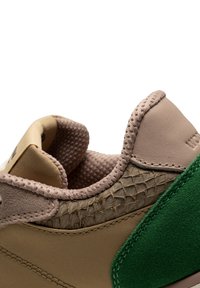 Zapato con un cuerpo de cuero marrón claro, acentos de tela verde y un panel lateral texturizado similar al reptil en beige; forro interior acolchado visible.