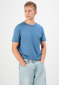Kék pamut póló kerek nyakkal és rövid ujjakkal, világos mosású farmernadrággal párosítva. Egyszerű dizájn, sima textúra, minták nélkül.
