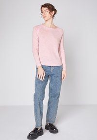 Helles rosa Langarmshirt mit rundem Kragen, kombiniert mit hellblauen geraden Jeans und schwarzen Plateauschuhen.