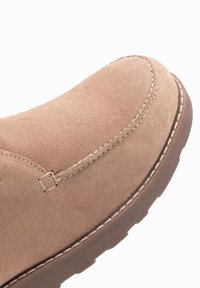 Zapato de ante beige con punta redondeada, perfil elevado, costuras en contraste blancas y suela de goma marrón.