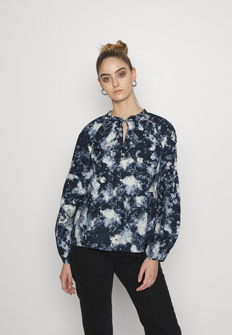 Blusa azul-marinho e branca com padrão, de decote redondo e detalhe em buraco. Apresenta mangas longas e bufantes, e um corte relaxado.