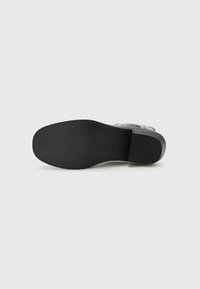 Suela de zapato negra, textura suave, forma rectangular, ligeramente elevada. Diseño simple, sin patrones ni acentos visibles. Adecuada para varios estilos de calzado.